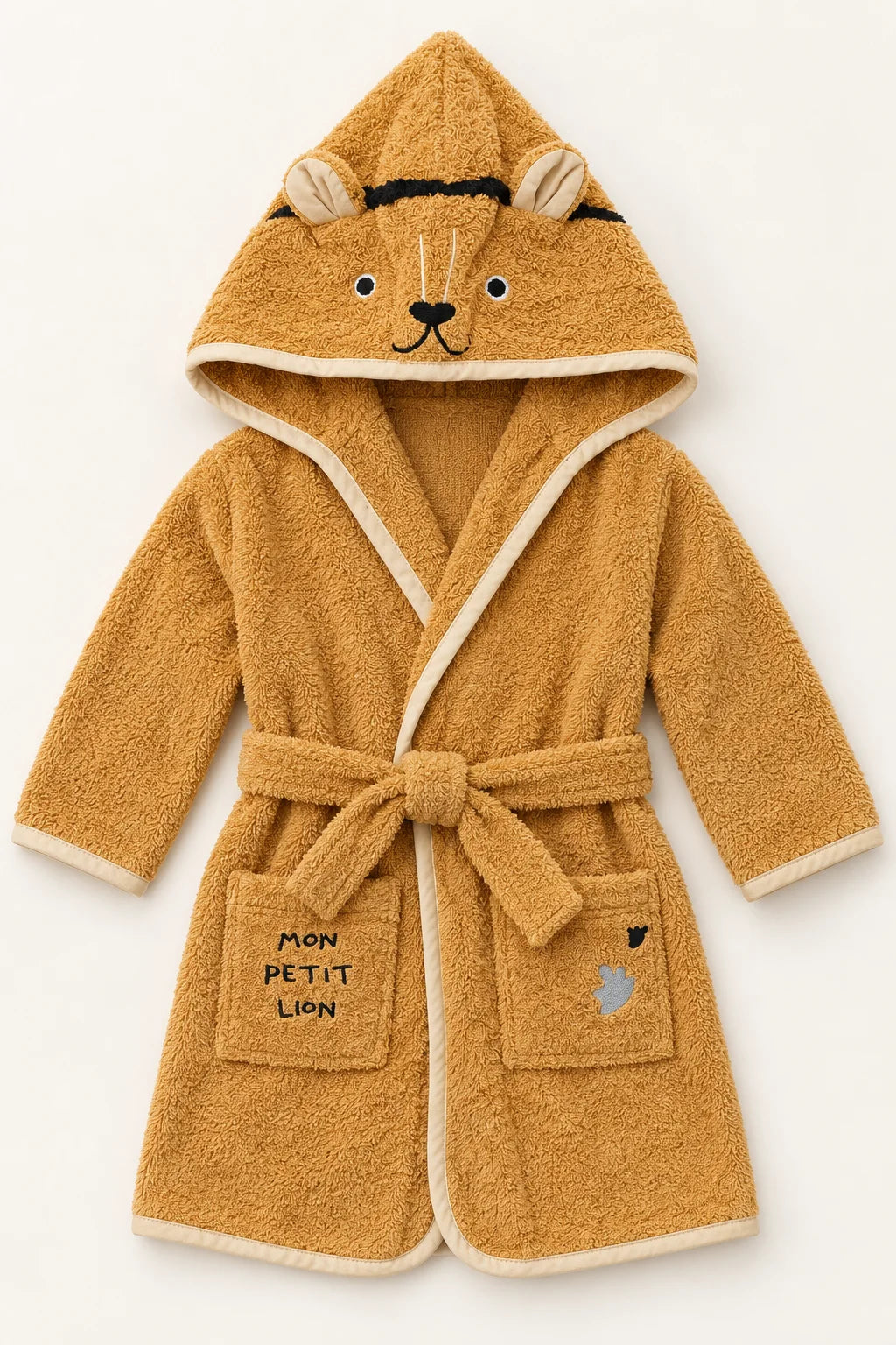 A plush hooded bathrobe for a child, styled like a lion cub, in a warm golden-brown terry cloth with cream trim. The hood features embroidered lion face details, and the front pockets are printed with 'MON PETIT LION'.